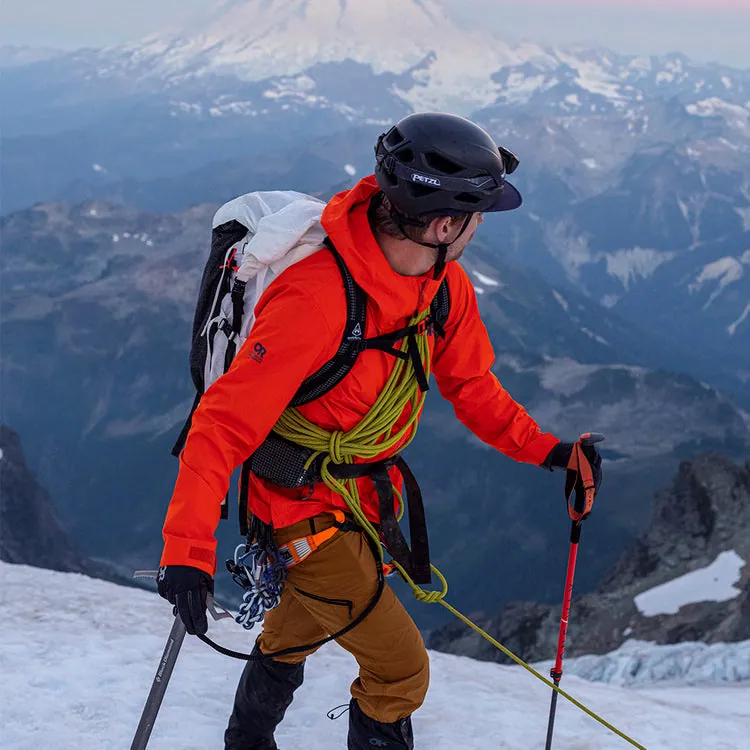 A mountaineer looks over their shoulder at the snow-covered mountain in the background.